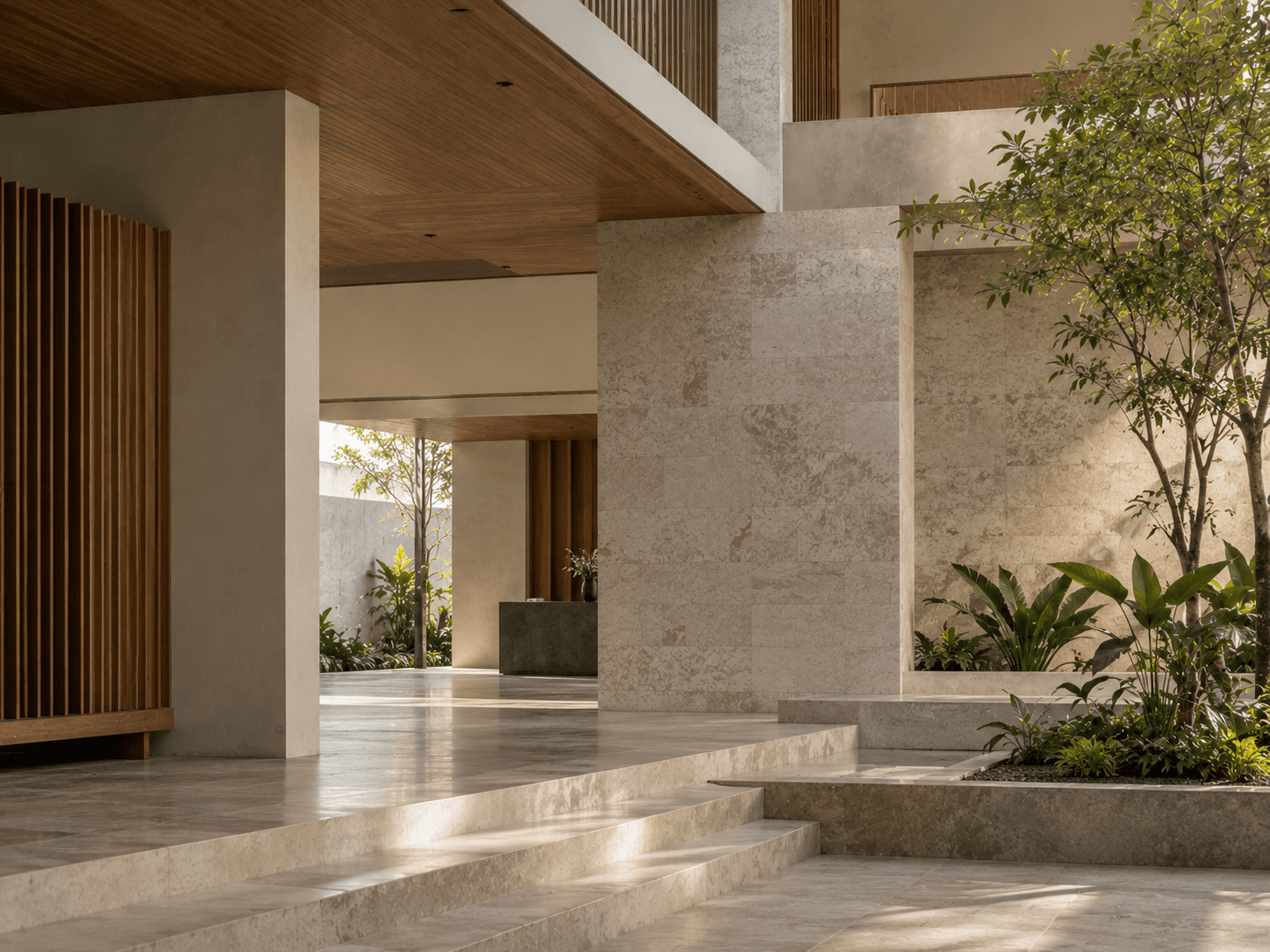 A stone atrium lobby with timber slats, low steps, and an indoor garden in soft daylight